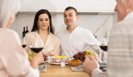 Young couple sitting at table drinking wine and having conversation with senior parentsの写真素材