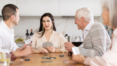 Joyful senior parents and young couple sitting around table playing poker