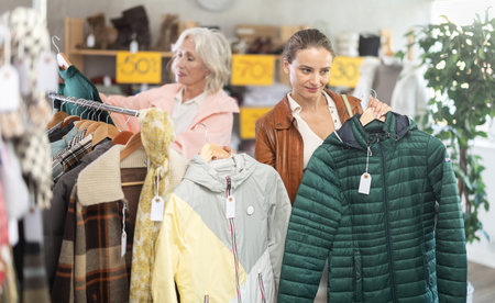 woman, together with a mature woman, chooses outerwear