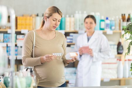 Pregnant woman choosing pills with help of pharmacistのeditorial素材
