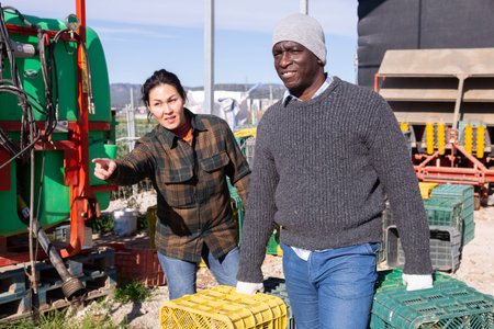 Female farmer giving instructions to worker carrying plastic crates