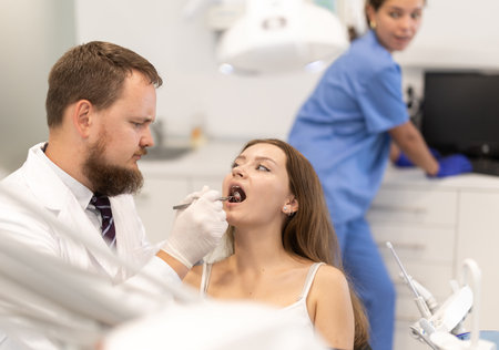 Male doctor checks young woman teeth during visit to dental clinicの写真素材