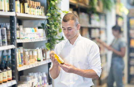 Thoughtful young man purchaser choosing cosmetic product in large supermarketのeditorial素材
