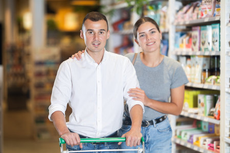 Couple with shopping cart browsing grocery shelves at supermarketの写真素材