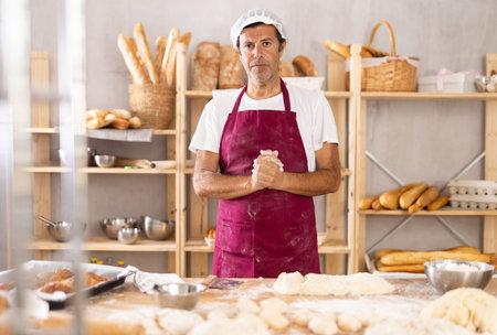Caucasian man cook-baker stands at table in kitchen of bakery
