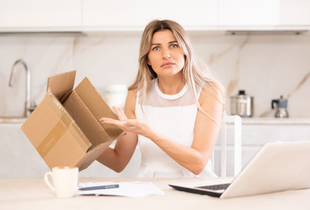 Wrong package. Unhappy woman with unpacked box in kitchen, sad about shipping mistake, frustrated...