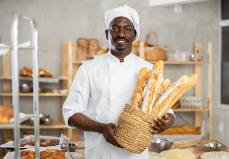 Portrait of experienced baker with tasty hot bread and baguettes in hands in kitchenの写真素材