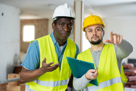 Two builders talking on indoor construction site