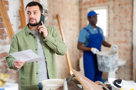Engineer of building under construction discussing repair plan on mobile phone