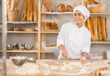 Young female baker cutting dough with scraper