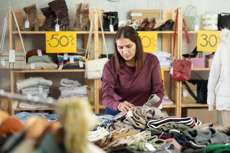 Selective Latina woman choosing trousers in clothing store