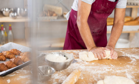 Professional male baker hands kneading dough in bakery