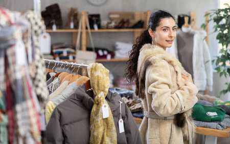 Female shopper chooses beautiful fur coat in clothing store