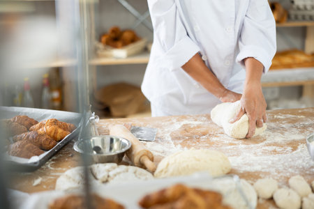 Cute doughs arranged on table in bakery with close-up of female hands skillfully kneading dough at...