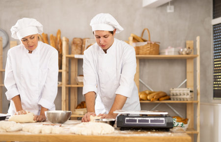 Male and female bakers kneading dough in workshop