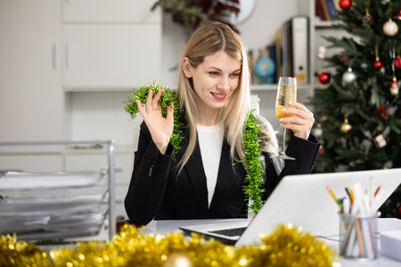 Business woman with a glass of champagne congratulates Merry Christmas on the Internet in officeの写真素材