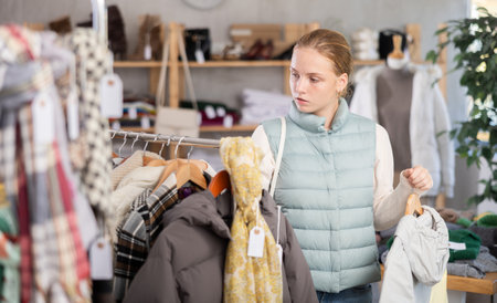 Attentive teenage girl choosing lightweight jacket in clothing storeの写真素材