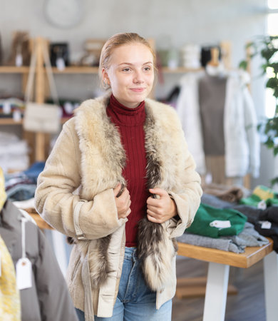 Positive teen girl trying on fur coat in clothing storeの写真素材