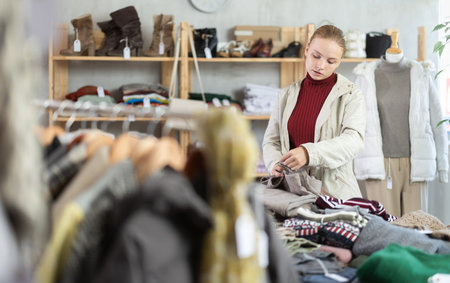 Selective teen girl choosing trousers in clothing store