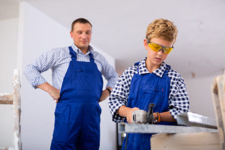 Young boy using tool in construction site, helping his father
