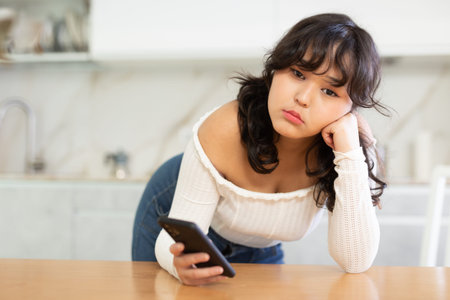 Sad young girl waiting for call from boyfriend in home interior