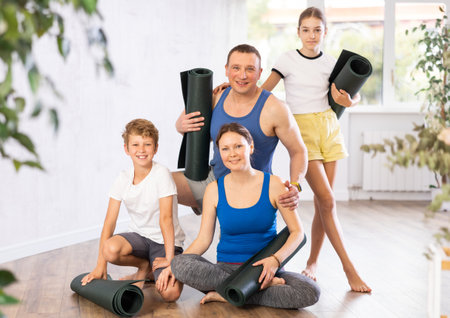 Happy mother and father with teen daughter and son hugging each other and posing with gymnastic mats before yoga class in studioの写真素材