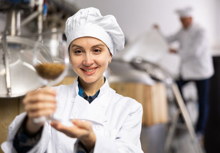 Portrait of positive female brewer with a glass of barley at breweryの写真素材