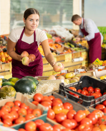 Friendly salesgirl offering ripe apples in fruit and vegetable storeの写真素材