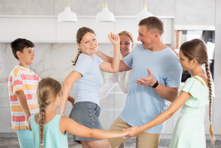 Children stand around their dancing parents in kitchen.の写真素材