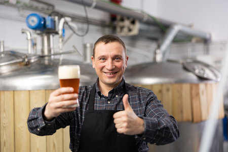 Brewer is standing with beer with foam in glass on his workplaceの写真素材