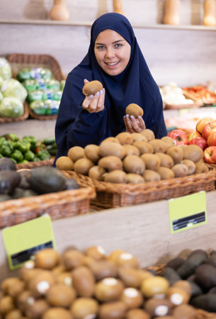 Young european woman in muslim dress choosing kiwis in storeの写真素材