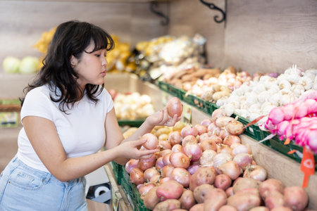 Young asian girl choosing onions on produce display i storeの写真素材