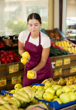Smiling girl seller is showing assortment of apples in vegetable shopの写真素材