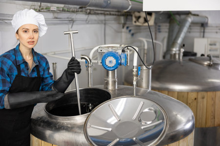 Female brewer is controls the brewing process near reservoir with beerの写真素材