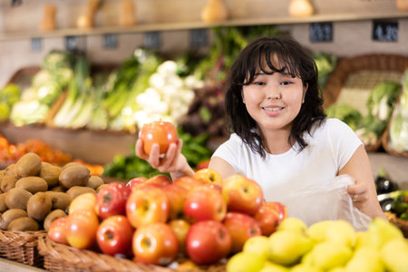 Delighted young woman purchaser choosing apples in grocery storeの写真素材
