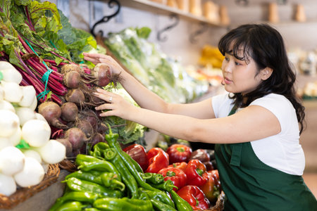 Young asian salesgirl arranging fresh beets on vegetable displayの写真素材