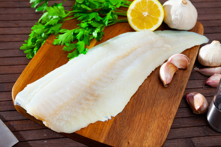 Raw codfish fillet on wooden table with condiments