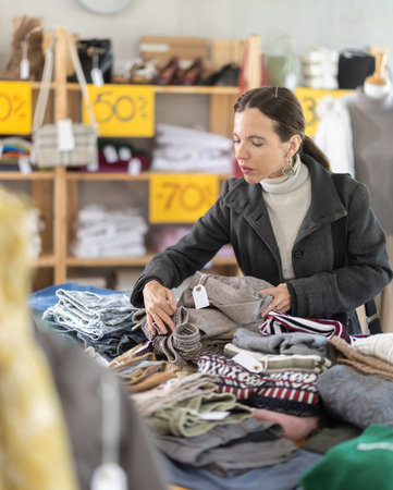 Selective middle-aged woman choosing trousers in clothing store