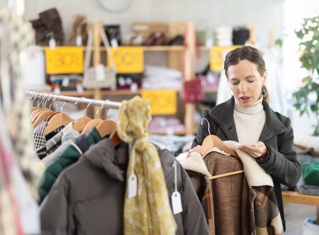 Woman chooses checkered jacket searches for fashionable clothes in clothing boutiqueの写真素材