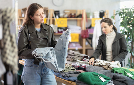 Female shopper chooses fashionable jeans trousers for autumn winter season in storeの写真素材