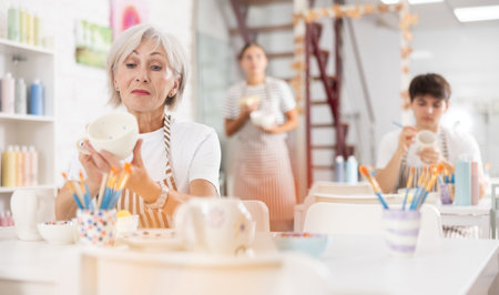 Experienced female artist painting ceramic cup in pottery workshopの写真素材