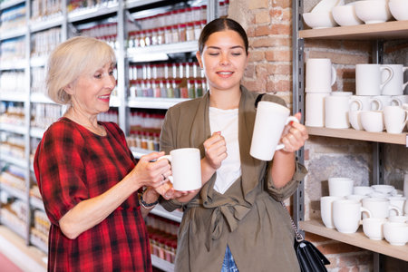 Two women choose mugs or cups together in pottery and ceramics shopの写真素材