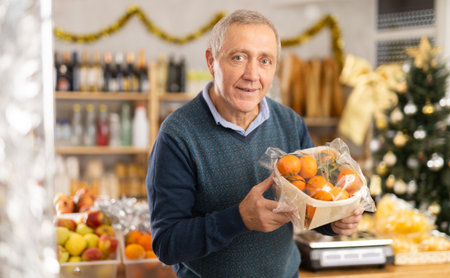Elderly man prepares to celebrate Christmas by choosing sweet tangerines in the produce section of supermarketの写真素材