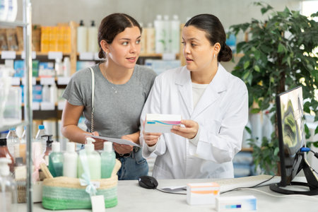 Young female pharmacist working on computer Asian client standing behind in chemistryの写真素材