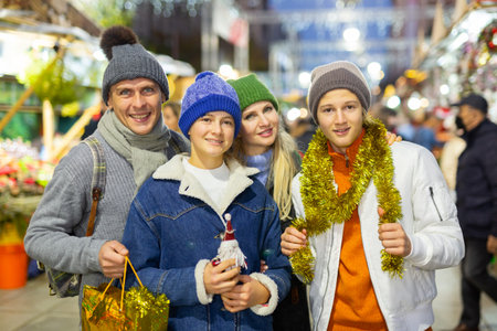 Portrait of happy family with christmas tinsel and gifts at street fair