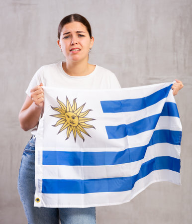 Sad young woman holding Uruguay flag against unicoloured backgroundの写真素材