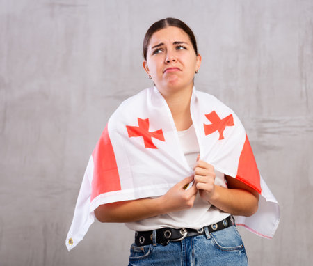 Stressed out sad young woman with flag of Georgia against gray wallの写真素材