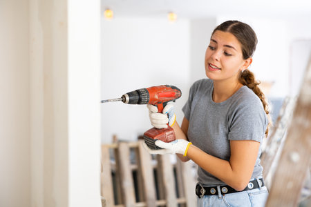 Woman drilling hole in wall in repairable roomの写真素材