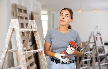 Portrait of young woman with drill in apartment