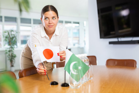 Positive young woman putting little flag of Japan on table next to the flag of Pakistanの写真素材